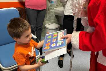 św. Mikołaj podaje chłopcu książkę, z tyły mama robi im zdjęcie