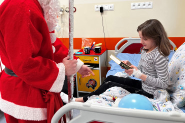Święty Mikołaj podaje książkę dziewczynie siedzącej na łóżku szpitalnym